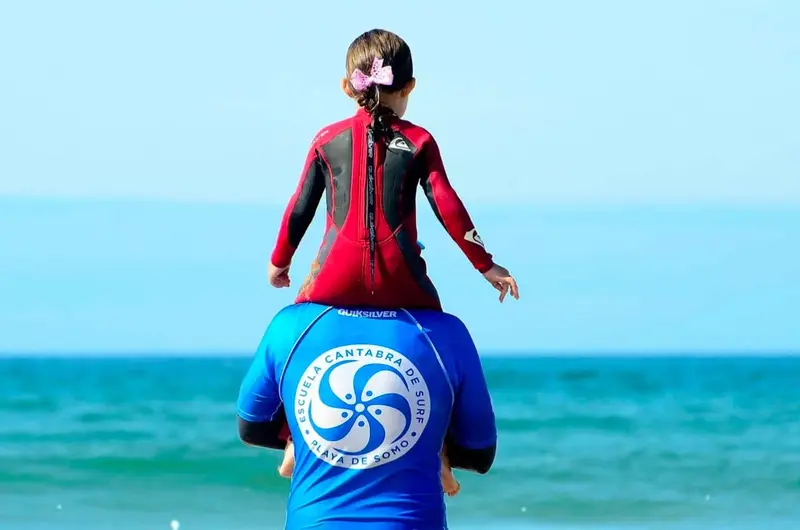 profesor de escuela cantabra de surf de espalda con una niña mirando al mar