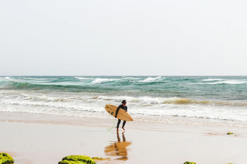 niño con tabla de surf caminando sobre la arena
