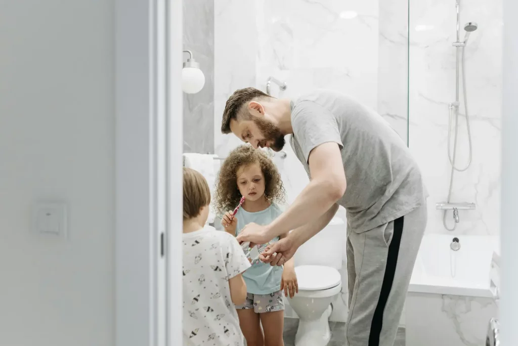 Ansiedad vuelta al cole. Hombre ayudando a los niños a lavarse los dientes.